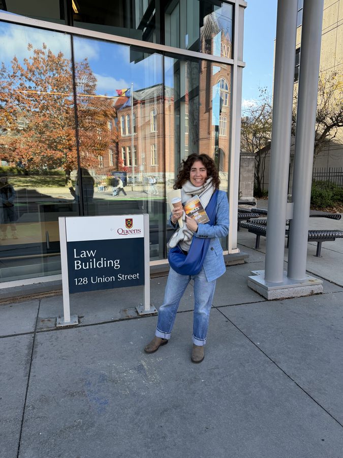 Alison Beder Solway outside the Queen's University Law Building, 128 Union Street, holding a copy of The Miles We Run